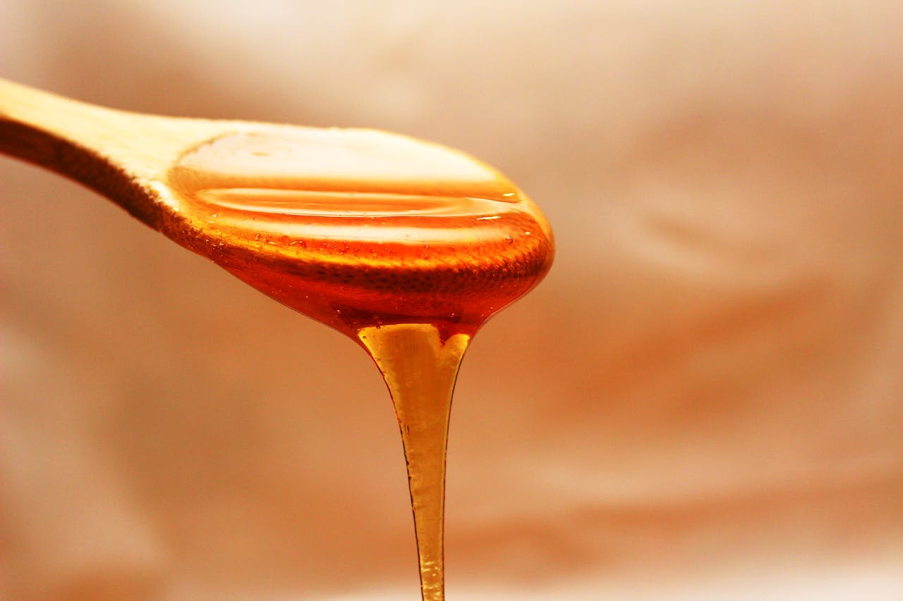 creative-approach-img Close-up of honey dripping from a wooden spoon, showcasing its rich texture and color.